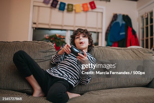 Boy playing video game while sitting on sofa at home,Victoria,British Columbia,Canada Boy playing video game while sitting on sofa at home,Victoria,British Columbia,Canada