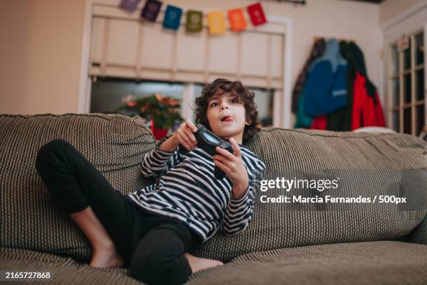 boy playing video game while sitting on sofa at home,victoria,british columbia,canada - videospel stockfoto's en -beelden