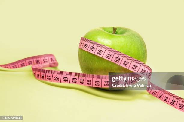 measuring tape wrapped around a green apple against trendy pastel green color background. - vitamina c foto e immagini stock