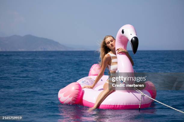 young woman sunbathing on a pink flamingo in the middle of the sea - plastic flamingo stock pictures, royalty-free photos & images
