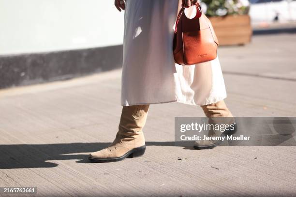 Isabella Höcherl is seen wearing a cream-white midi skirt, an orange leather bag, and suede sand-colored western boots with embroidery from...