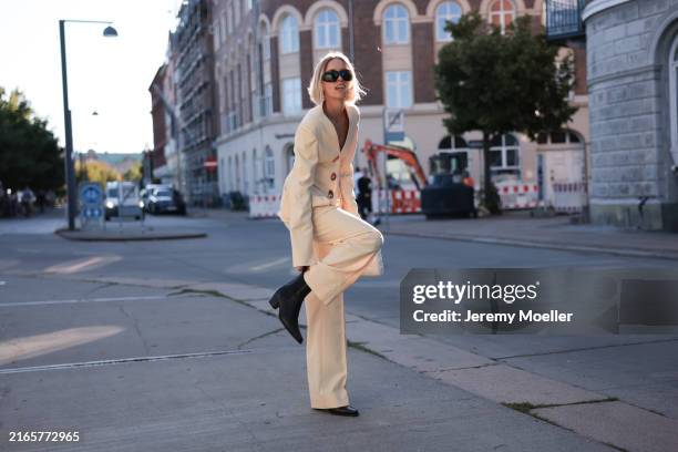 Hannah Stefansson is seen wearing black sunglasses, a light yellow suit, a white leather bag, and pointed black Chelsea boots from Copenhagen Studios...
