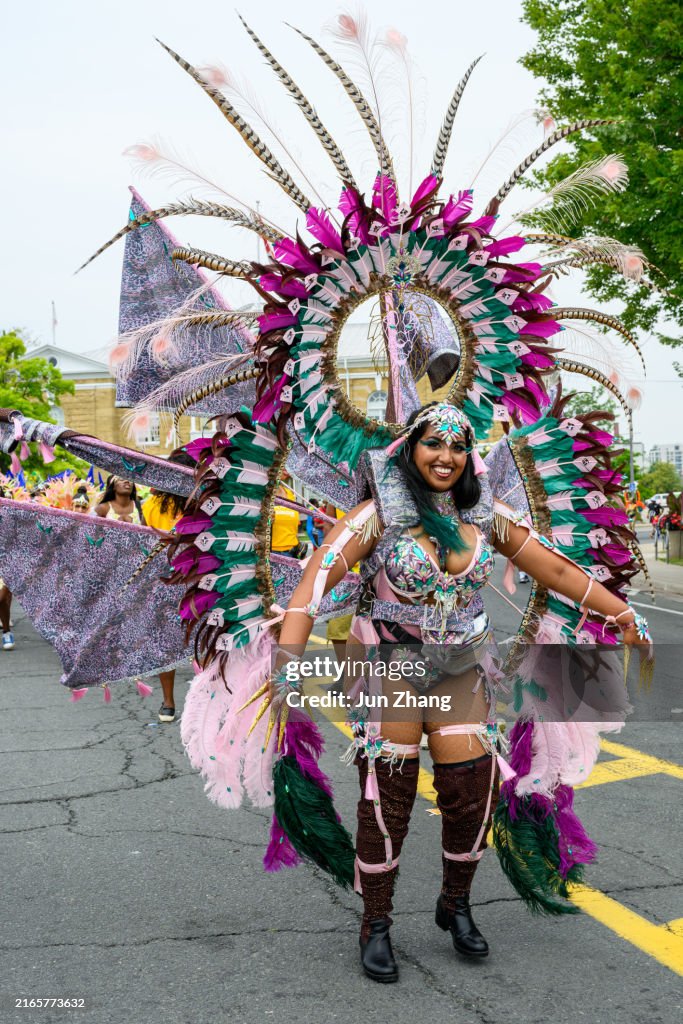 Toronto 2024 Caribbean Carnival: Smiling performer in feather costume walks into the venue of the event