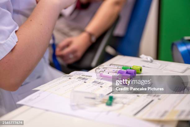 medical professional in a white coat handling blood sample tubes over paperwork at a laboratory station - blood collection tube stock pictures, royalty-free photos & images
