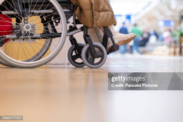close-up of a wheelchair with a person's legs, indoors with a blurred background of a public space - persons with disabilities stock pictures, royalty-free photos & images