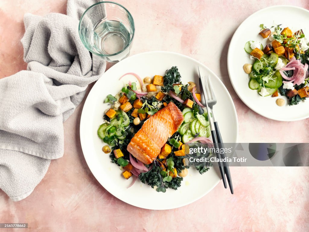 Plate of roasted salmon with fresh salad on pink background