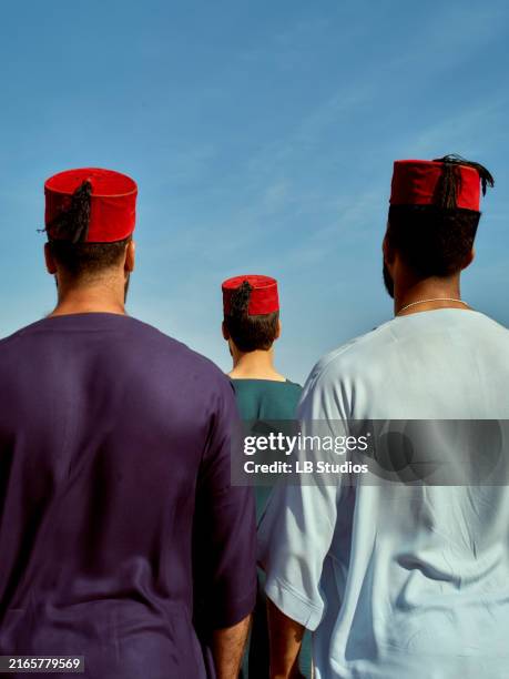 three individuals wearing traditional red hats and colorful clothing standing against a clear blue sky - red hat stock pictures, royalty-free photos & images