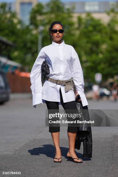 Guest wears black sunglasses, white button up long sleeve shirt, black leather handbag, light brown belt, black capri pants, shiny black leather...