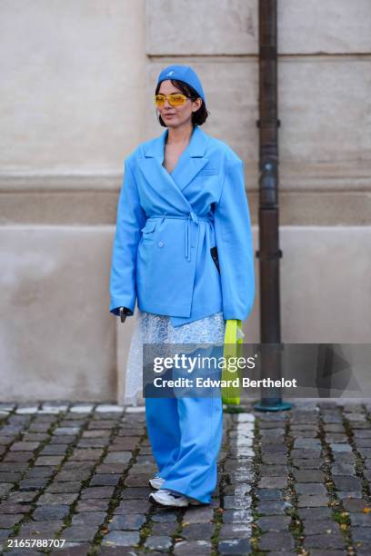 Guest wears bright blue hat, bright blue blazer trench coat, yellow sunglasses, white lace skirt, bright blue loose pants, bright lime green Coperni...