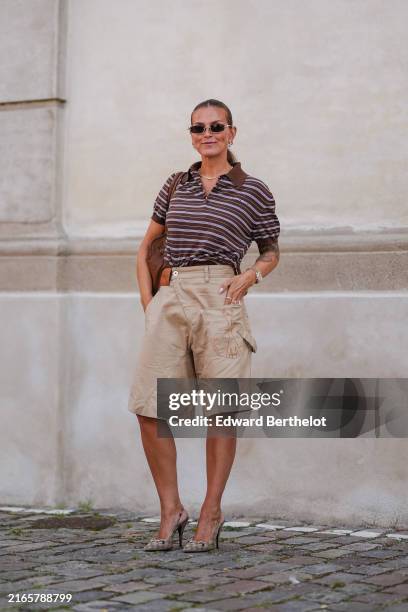 Janka Polliani wears black sunglasses, silver earrings, silver necklace, dark brown light gray striped short sleeve shirt, light brown leather bag,...