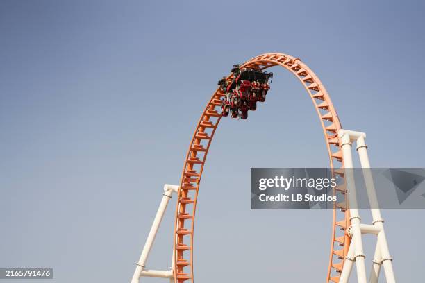 roller coaster at the peak of a loop against a clear blue sky - montaña rusa fotografías e imágenes de stock