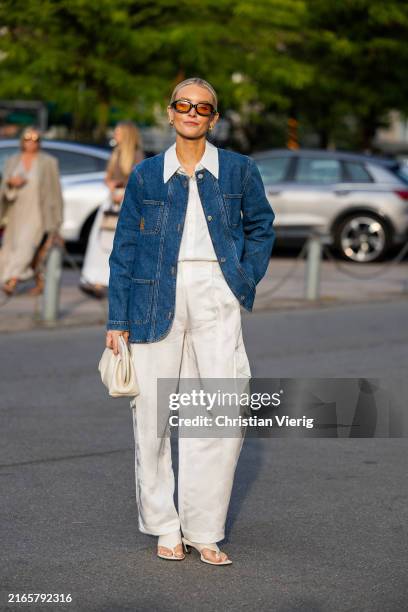 Polly Sayer wears denim jacket, white pants with side pockets, button shirt, bag outside Baum & Pferdgarten during day three of the Copenhagen...