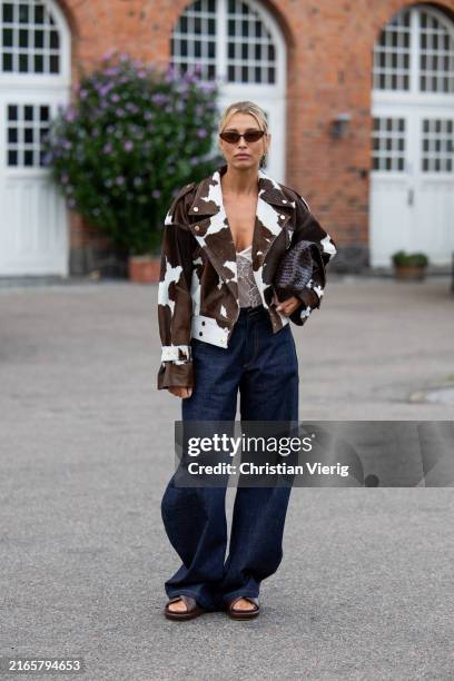 Guest wears brown cow print jacket, dark denim jeans outside Baum & Pferdgarten during day three of the Copenhagen Fashion Week SS25 on August 07,...