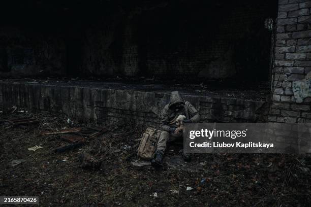 A man in dark green camouflage and a gas mask sits among the ruins of the city.