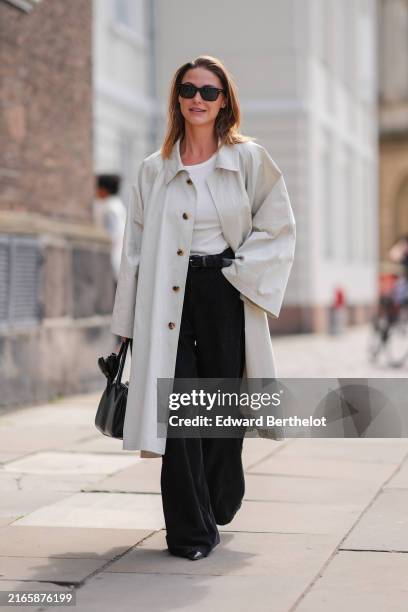 Sophia Roe wears black sunglasses, white t-shirt, cream trench coat, black pants, black leather bag, outside Mark Kenly Domino Tan, during the...