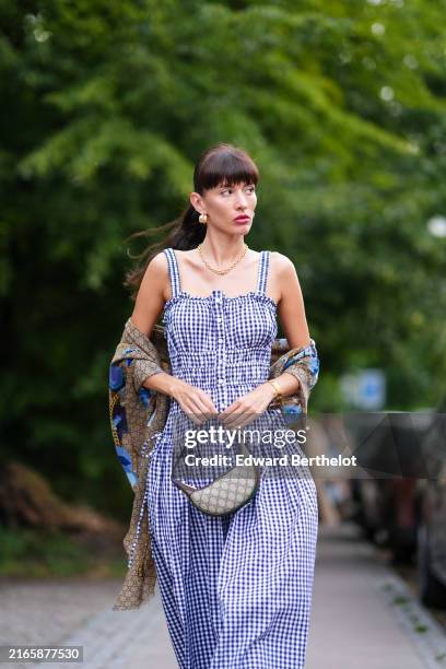 Katya Tolstova wears gold earrings, gold necklace, white and blue pattern midi dress, dark brown blue floral pattern/print Gucci scarf, light gray...