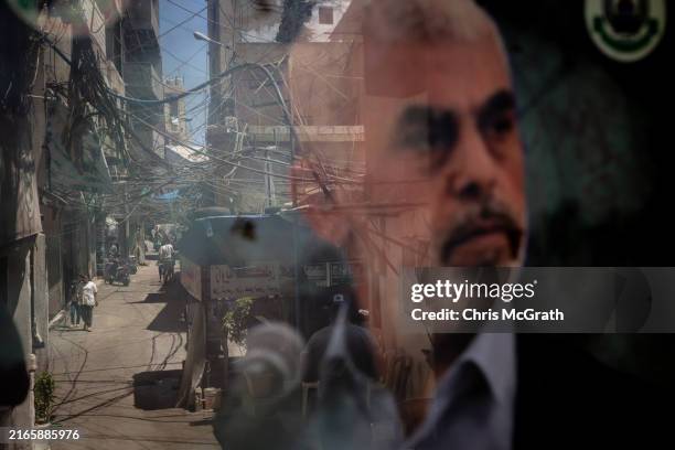 People are reflected in a window displaying a poster of newly appointed Hamas leader Yahya Sinwar in the Palestinian camp of Bourj al-Barajneh on...