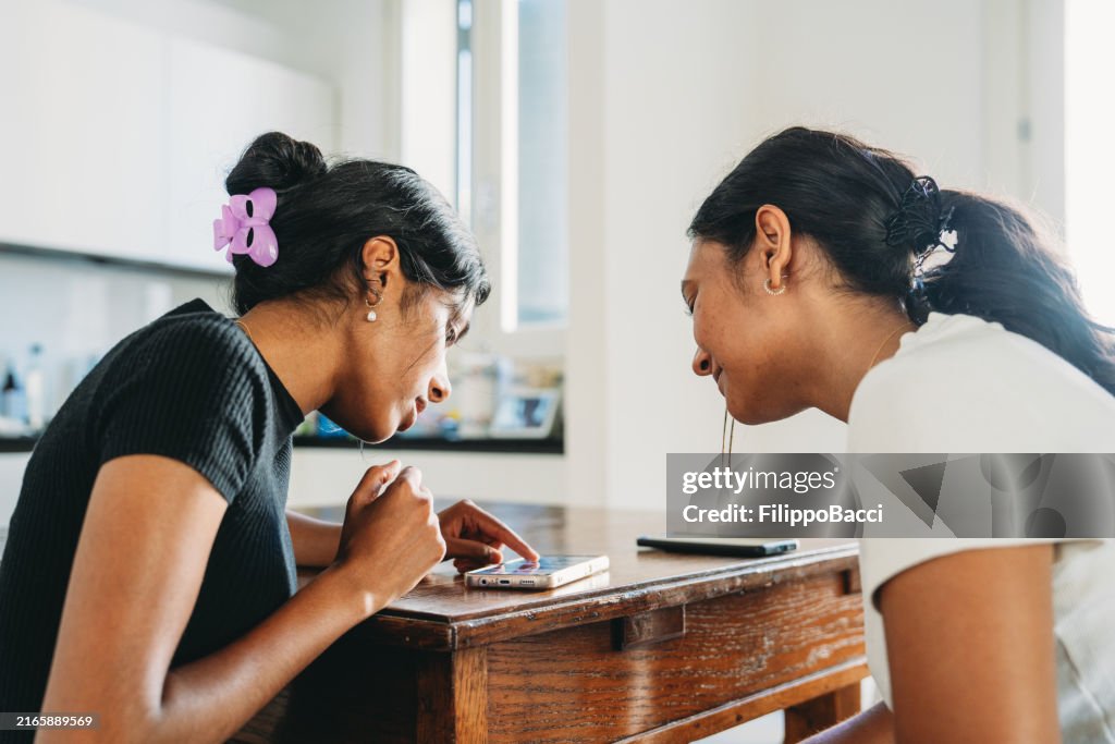 Two teenage girls sharing smartphone at home