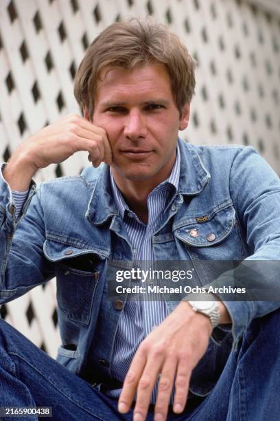 American actor Harrison Ford, wearing a denim jacket over a blue-and-white striped shirt, his head resting against right hand, United States, March...