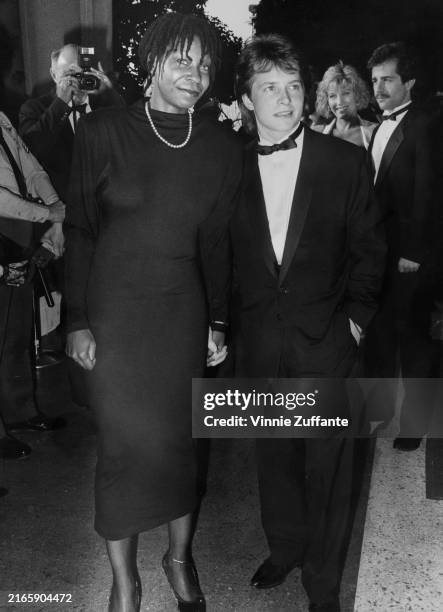 American actress and comedian Whoopi Goldberg, wearing a black outfit with a pearl necklace, and Canadian actor Michael J Fox, who wears a tuxedo and...