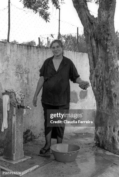 View of an unidentified woman as she washes clothes in basin at a public tap in the Restelo neighborhood, Lisboa, Portugal, 1990.