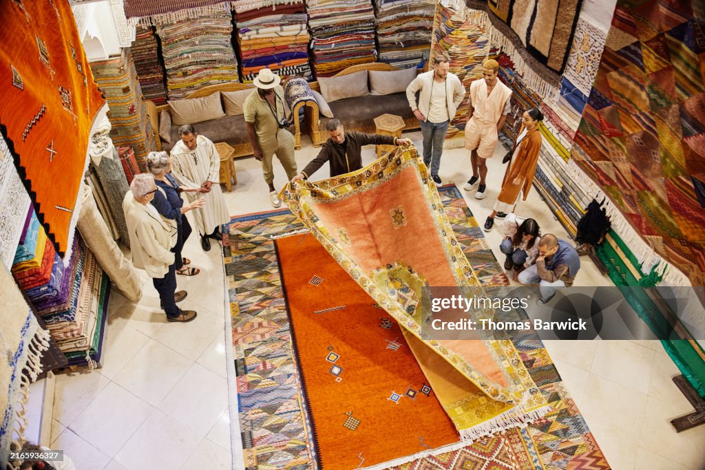 Extreme wide overhead shot salesman opening rug for customers at shop