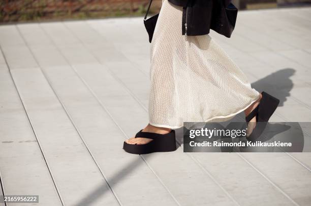 Sophia Geiss wears a long beige knitted maxi dress, black flip flops, sandals, leather jacket and black bag during day four of the Copenhagen Fashion...