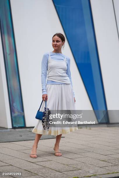 Guest wears light blue long sleeve shirt, white tank top, white with yellow bottom midi skirt, dark blue leather bag, navy blue white floral scarf,...