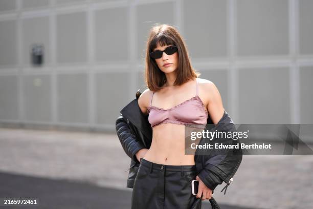 Guest wears black sunglasses, dark pink bralette, black biker leather jacket, shiny black midi leather skirt, outside Munthe, during the Copenhagen...