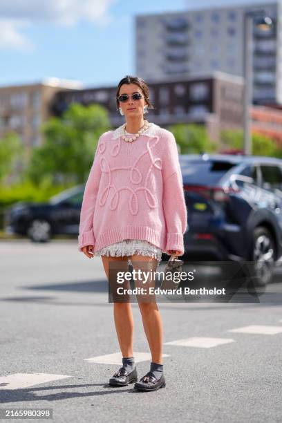 Guest wears black sunglasses, silver earrings, cream beaded necklace, light pink pattern oversized wool sweater pullover, white pattern mini skirt,...