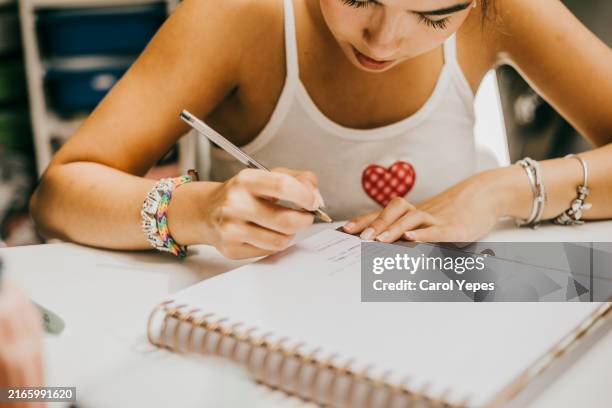 young woman concentrated as she write in a ruled notebook, possibly for planning, journaling, or note-taking. - organizador personal fotografías e imágenes de stock