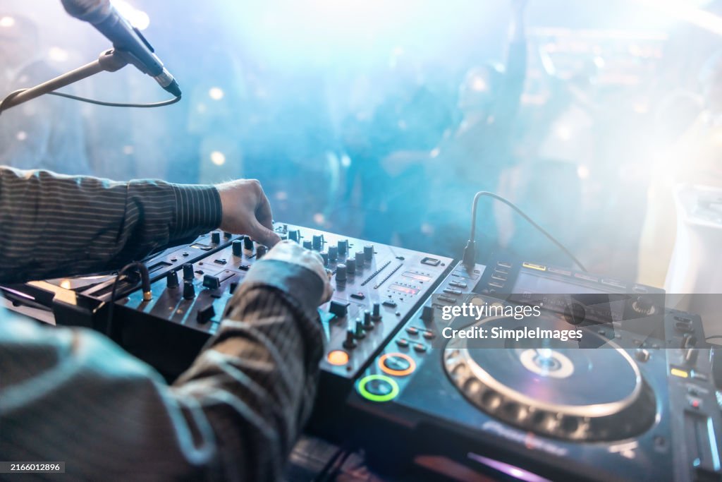 Close up of DJ hands controlling a music table in a night club. Night club, nightlife concept. DJ hands hold microphone and mixing DJ remote. Neon light.