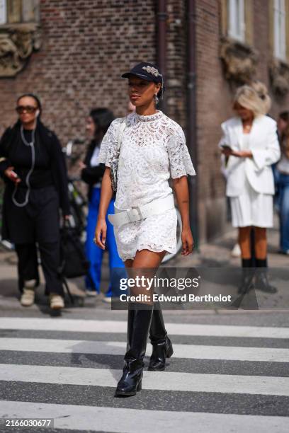 Guest wears black baseball cap with light brown detail, silver earrings, white sheer mesh lace short sleeve mini dress with floral emrboidery, white...