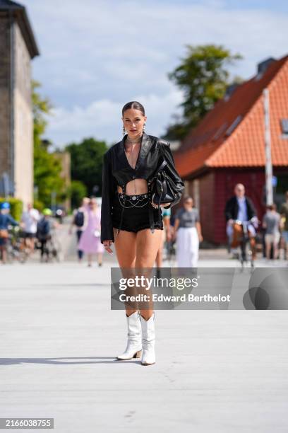 Guest wears silver earrings, silver necklaces, shiny black cropped leather blazer jacket, black mini shorts black belt, shiny black leather bag,...