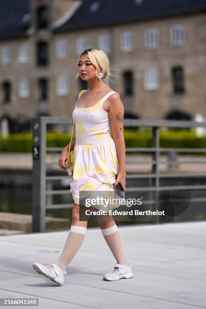 Guest wears silver earring, light pink yellow pattern mini dress, yellow bag, white sheer mesh socks, white sneaker shoes, outside Marimekko, during...