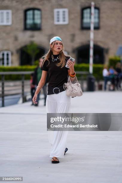Guest wears white blue pattern head scarf, gold necklace, black high neck short sleeve shirt, orange bangles, silver bracelet, black leather belt,...