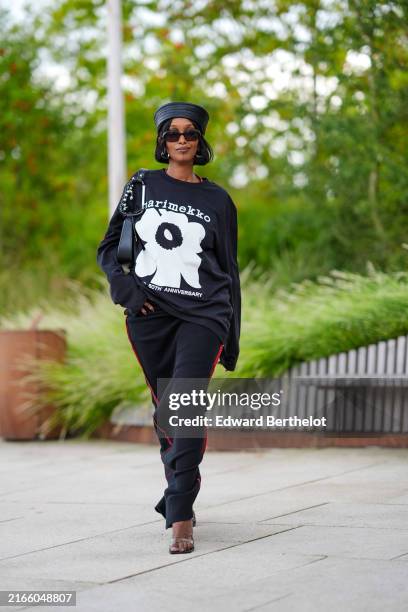 Guest wears black hat, black sunglasses, black earrings, black oversized long sleeve Marimekko graphic print shirt, black leather bag, black maxi...