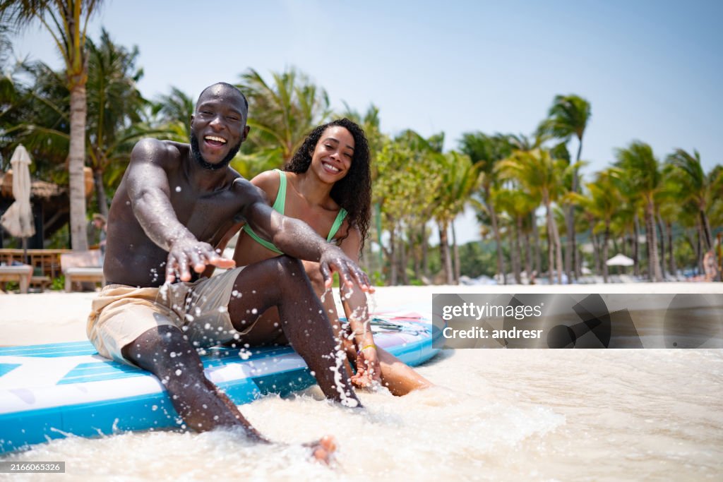 Coppia che si gode le vacanze in spiaggia provando paddleboard