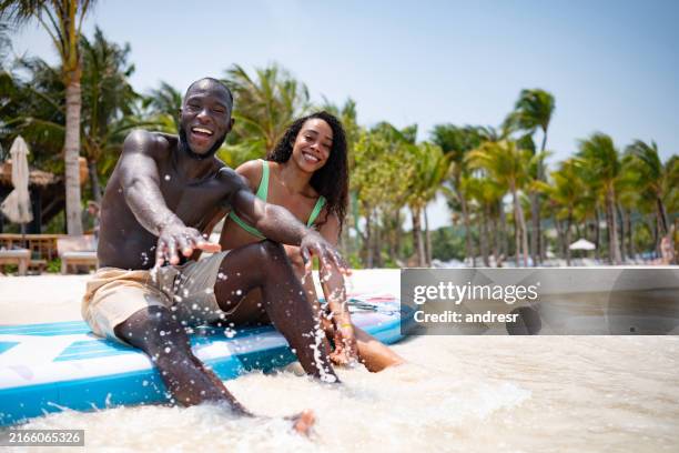 coppia che si gode le vacanze in spiaggia provando paddleboard - vacanza al mare foto e immagini stock