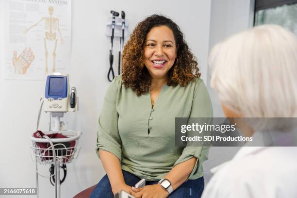 unrecognizable senior female doctor listens to mid adult female patient - dokterspraktijk stockfoto's en -beelden