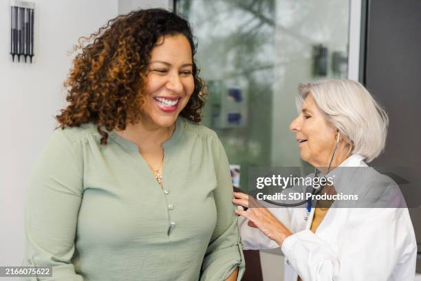 female patient laughs while female doctor listens to lungs - cuidados de saúde primários imagens e fotografias de stock