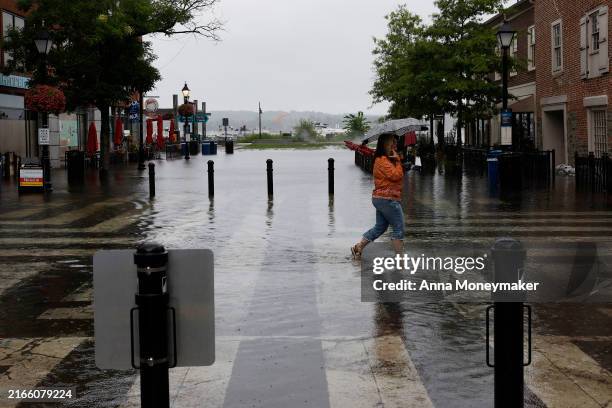 Woman speaks on her phone as she walks through high tide floodwaters in Old Town Alexandria on August 09, 2024 in Alexandria, Virginia. The...