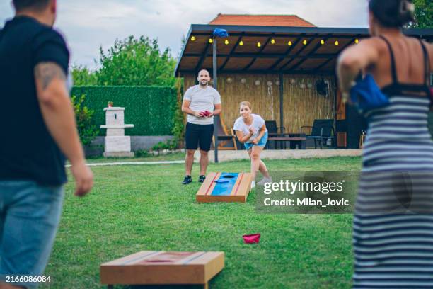 two couples playing bean bag toss in the backyard - playing corn hole stock pictures, royalty-free photos & images