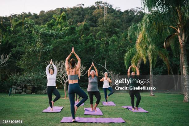 group of women practicing yoga outdoors with a instructor - yoga imagens e fotografias de stock