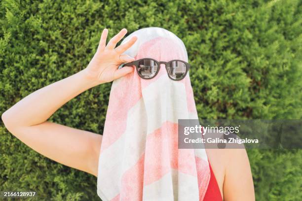 funny portrait of young woman in beach towel and sunglasses against green wall - envuelto en una toalla fotografías e imágenes de stock