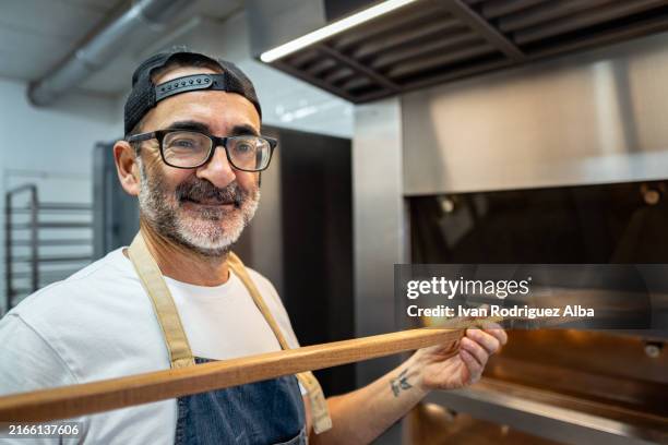 baker using a shovel to take bread from oven - inserting stock pictures, royalty-free photos & images