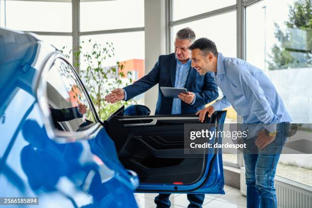 salesman helping the male customer to choose a new car - car salesperson stock pictures, royalty-free photos & images