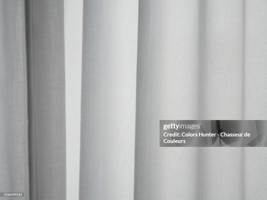 Close-up of a textured, backlit, wavy white curtain. Focus in the center of the photo.
Sunlight. Monochrome.
London, England, United Kingdom.