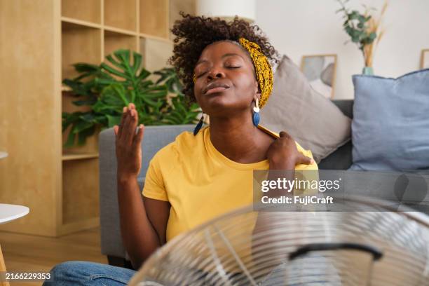 young woman sweating suffering summer heat wave at home - luchtvochtigheid stockfoto's en -beelden