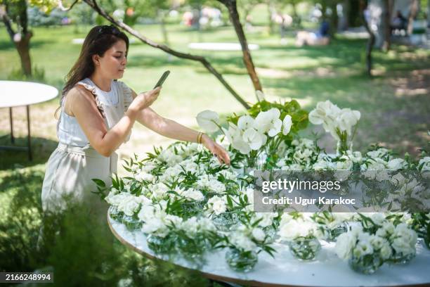 a woman from the wedding planning team is photographing the garland flowers on the wedding table. - photo messaging stock pictures, royalty-free photos & images